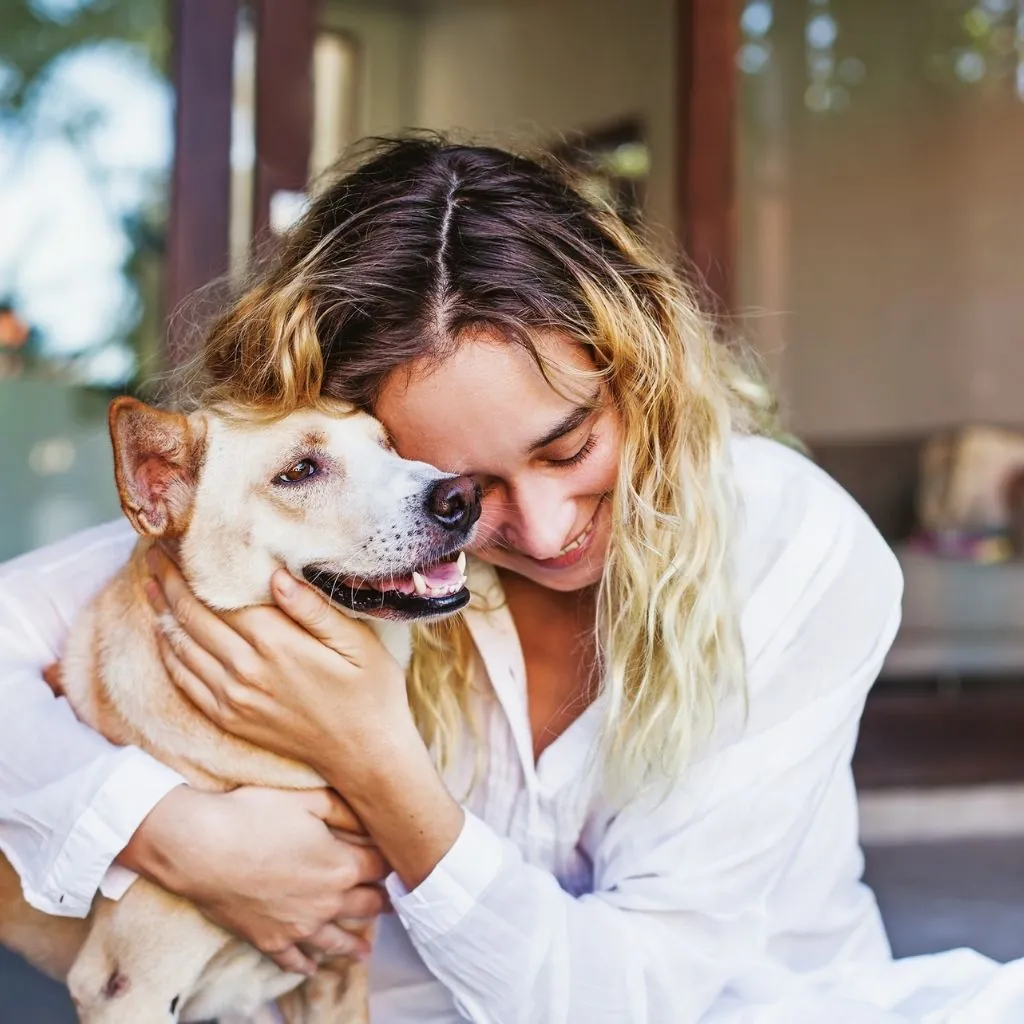 A smiling woman hugging a happy dog at home