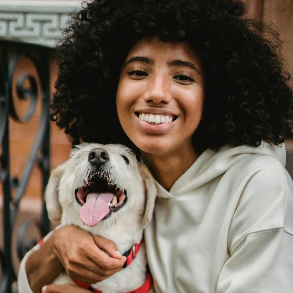 A smiling woman with curly hair hugging a white dog