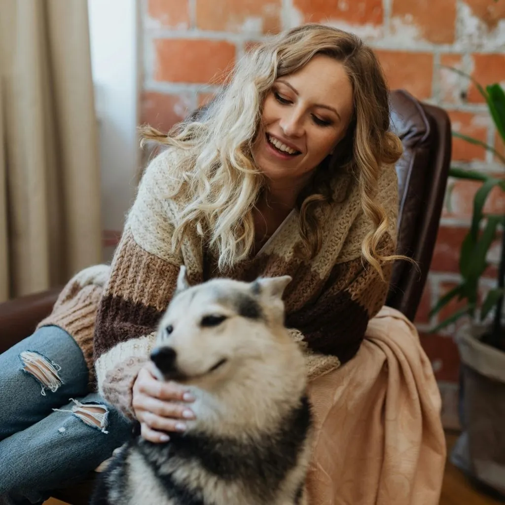 A woman relaxing in an armchair at home with a husky